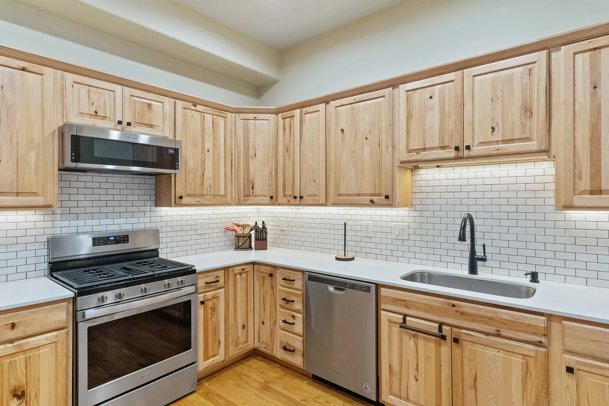 This image displays a kitchen with stainless steel appliances, handsome wood cabinetry, and a crisp white subway tile backsplash. The layout is spacious, allowing for easy movement and ample meal prep, while the modern design emphasizes both style and functionality. Warm lighting and visible counter space suggest a welcoming environment for cooking and entertaining.