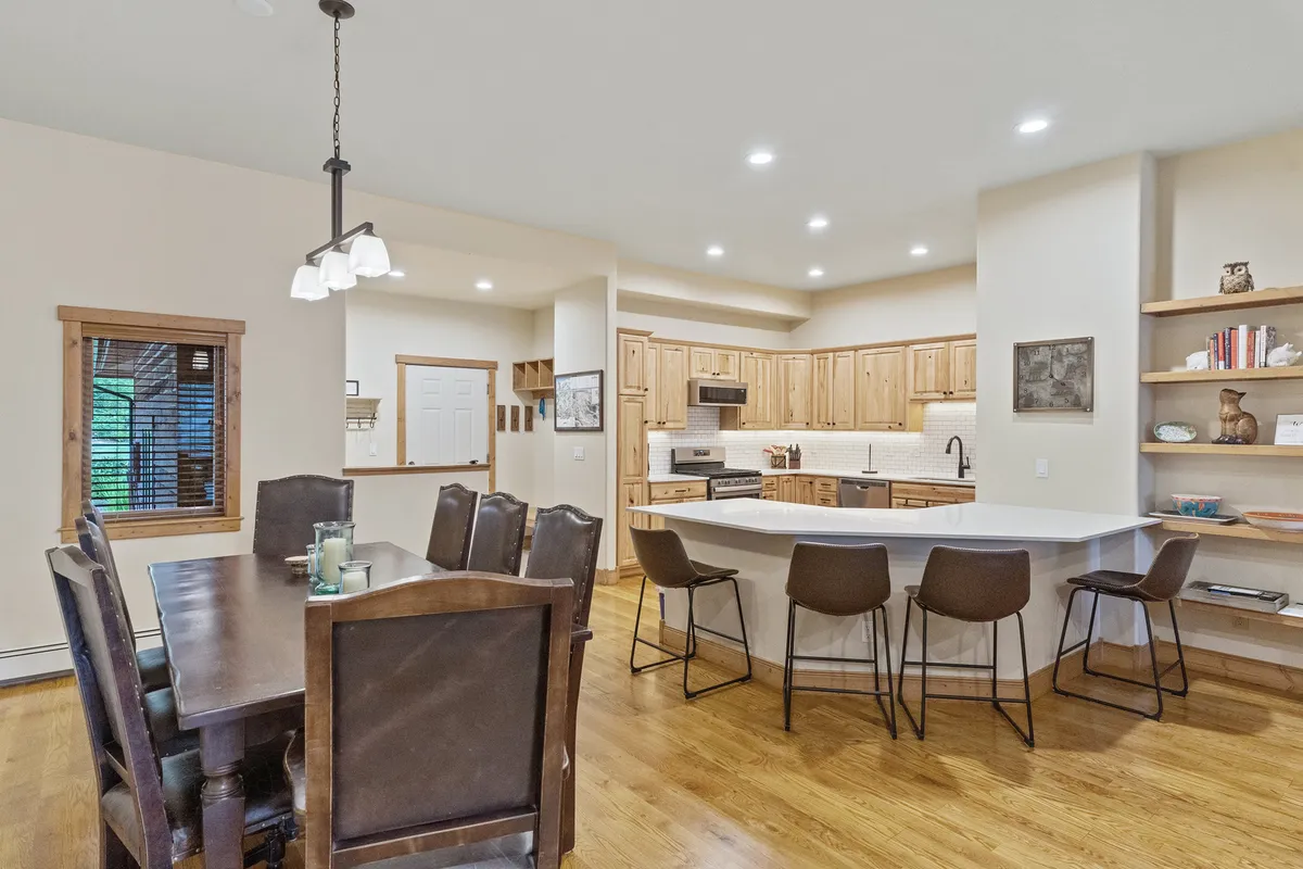 A spacious dining area with a large table and plenty of seating, adjacent to a kitchen with wooden cabinetry and open shelving. The setup is bright and inviting, perfect for lively group meals, celebrations, and family gatherings, as described in the section.
