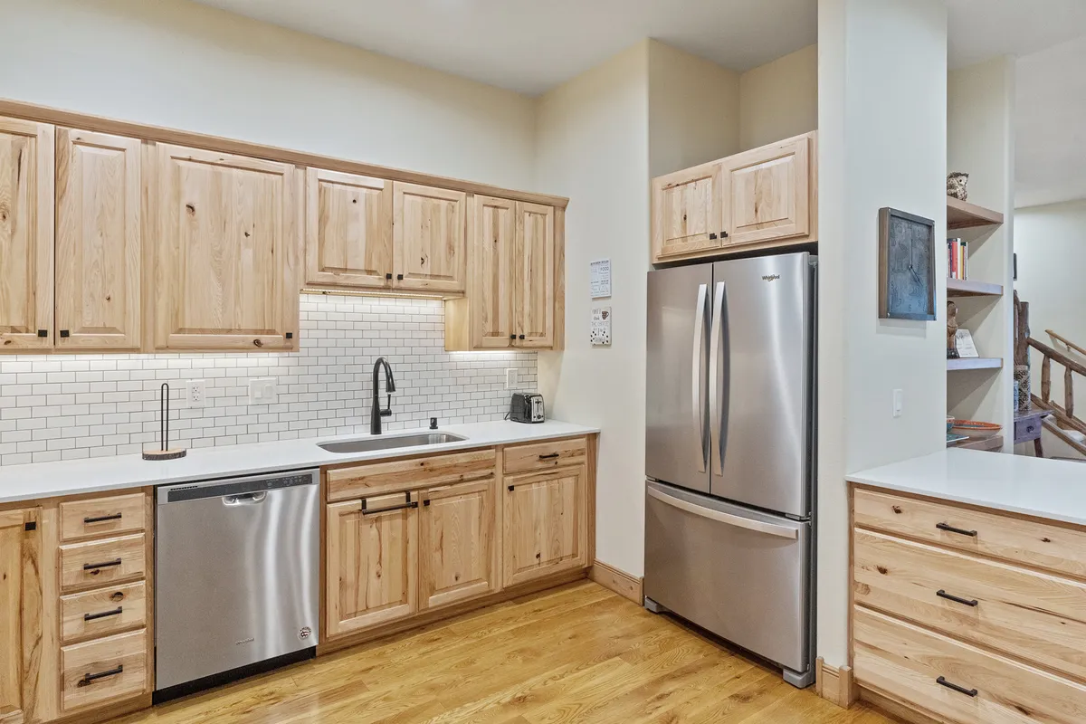 A view of a kitchen featuring wooden cabinetry, stainless steel appliances, and a white backsplash, with plenty of counter space for food preparation. The inviting setup emphasizes functionality and a cozy atmosphere, with hints of family gatherings or social cooking experiences.