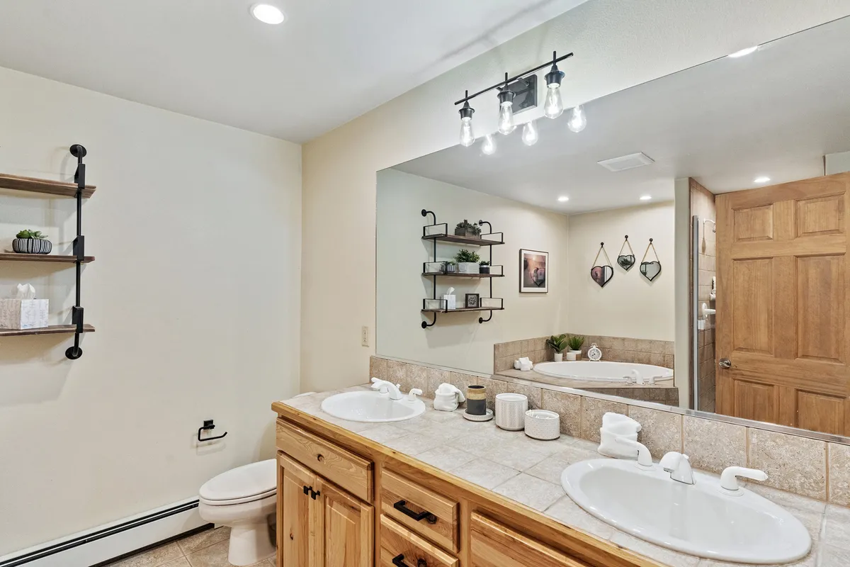 Here, a calming bathroom features a double sink vanity with wooden cabinetry, a large mirror, and a bathtub. Soft lighting and simple decorative elements create a spa-like atmosphere inviting relaxation and self-care.