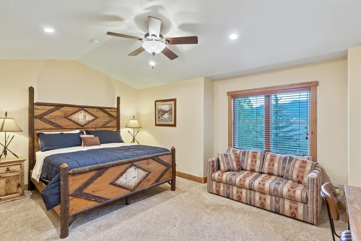 This image showcases a rustic wooden bed paired with a striped sofa, all bathed in natural light from a large window offering views outside. The space feels serene and comfortable, with décor that emphasizes relaxation and connection to the outdoors.