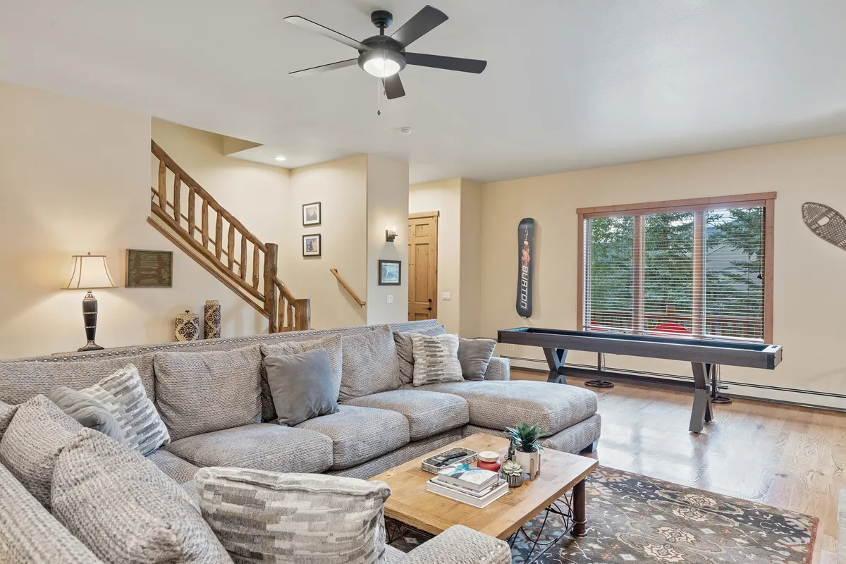 Featuring a large sectional sofa, a wooden coffee table, and a window streaming in natural light, this space feels open and inviting. The view through the window and the arrangement imply a seamless connection to the outside world, while also highlighting spaces for socializing and relaxing after outdoor adventures.