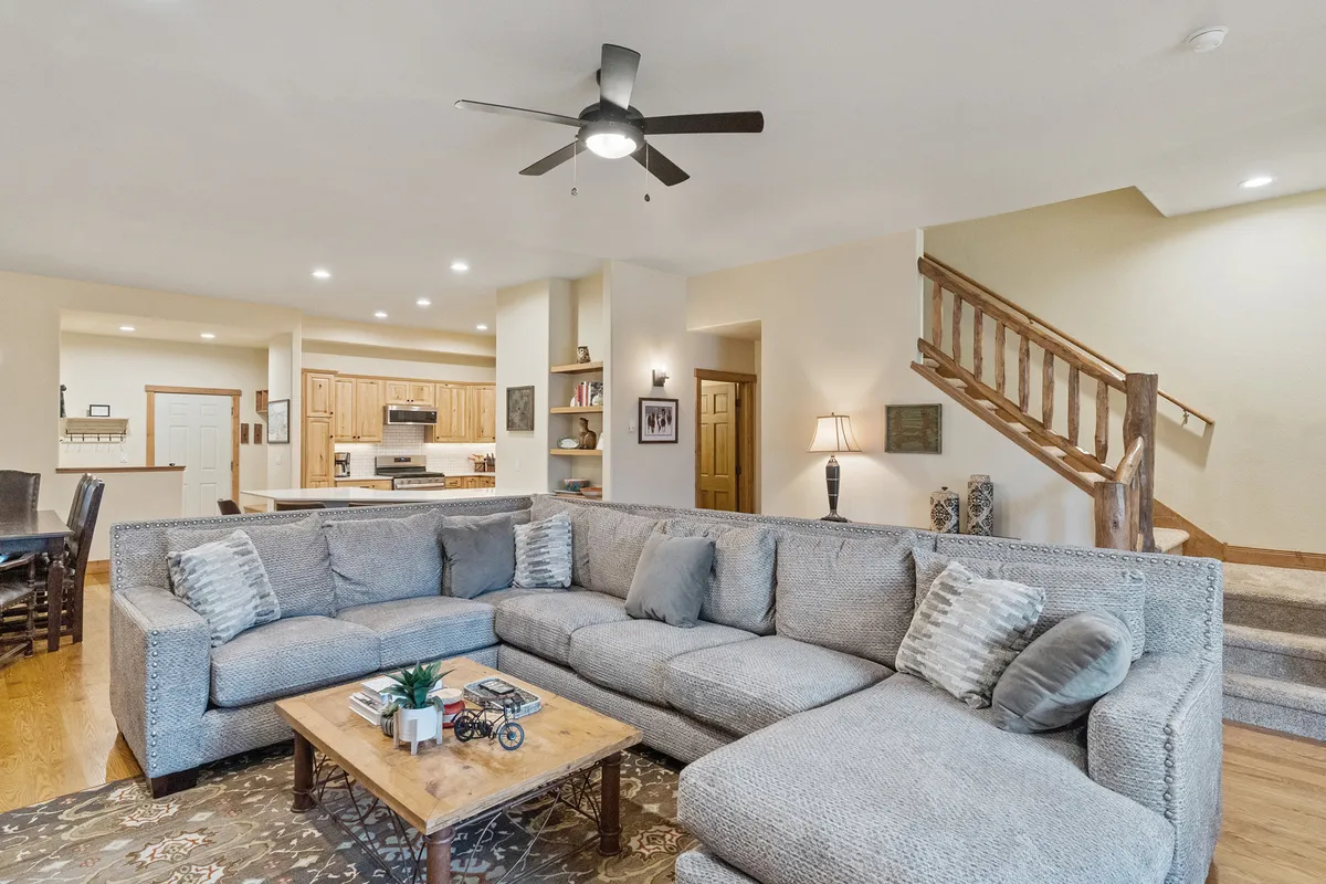 The image showcases a spacious, stylish living area featuring a plush sectional sofa, inviting coffee table, elegant lighting fixtures, and an open staircase—all arranged to encourage relaxation and togetherness. The ambiance is warm and cozy, perfect for gathering with family or friends for movie nights, games, or casual conversation.