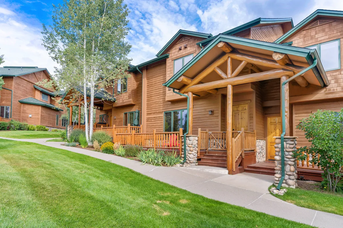 This image displays a wooden porch with stone accents, green landscaping, and a bright blue sky. The inviting atmosphere encourages relaxation, socializing with neighbors, and enjoying the outdoors. It visually connects the property to the walkable, community-oriented neighborhood described in the section.